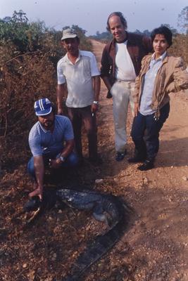 Pessoas posam em torno de jacaré, em pé de jaqueta marrom, Kim Esteve