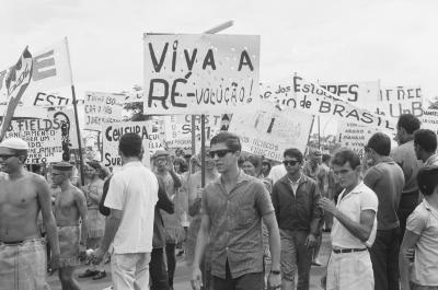 Calouros com roupa de estopa desfilam pela avenida W3 segurando cartazes como parte do trote da Universidade de Brasília