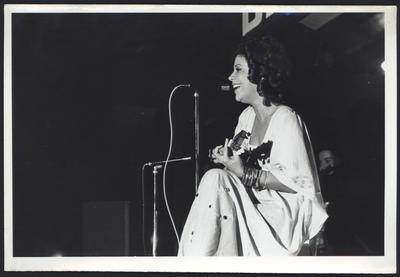 Beth Carvalho ao microfone com o cavaquinho