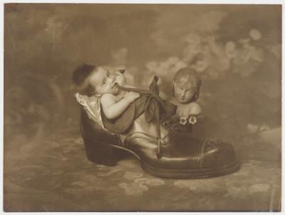 Retrato de criança envolta em bandeira brasileira, dentro de enorme pé de sapato.