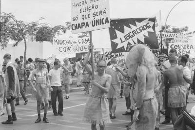 Calouros com roupa de estopa desfilam pela avenida W3 segurando cartazes como parte do trote da Universidade de Brasília
