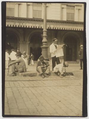 Ferroviário lê jornal, cercado por carregadores de malas,