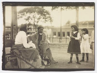 Duas mulheres, uma de costas, descansando em banco de praça