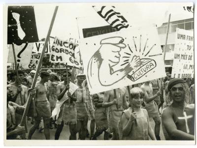 Calouros com roupa de estopa desfilam pela avenida W3 segurando cartazes como parte do trote da Universidade de Brasília