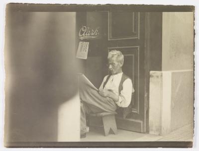 Homem lendo jornal na porta de estabelecimento comercial